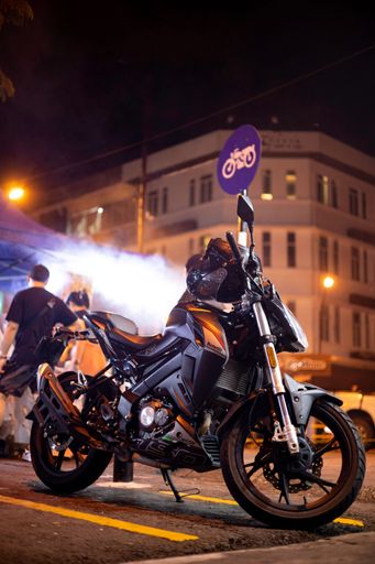 A vertical shot of a black bike parked on the side of the street at night
