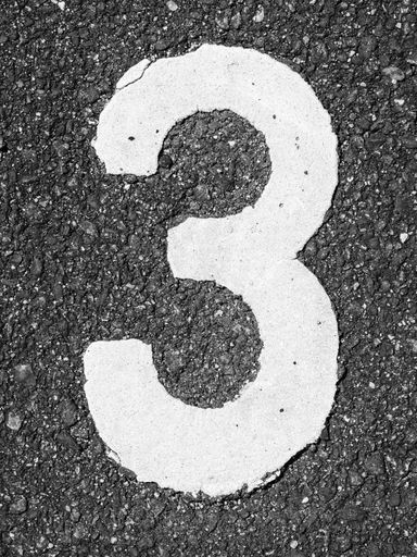 A vertical shot of a white number three on asphalt ground