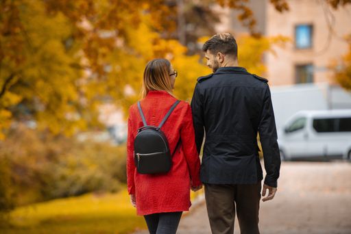 A couple holding hands and walking through a road surrounded by colorful trees during autumn