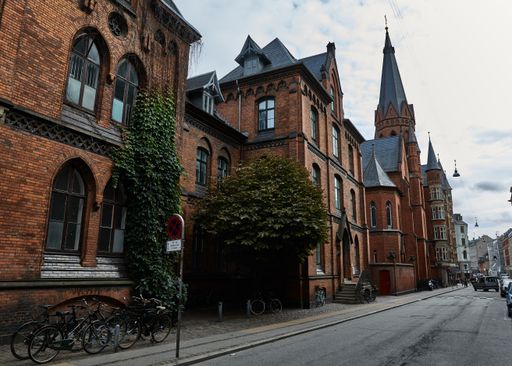 An ancient buildings with towers in a neighborhood surrounded by greenery bicycles and cars