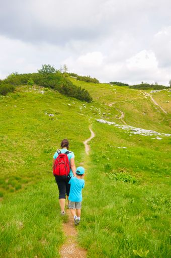 Small footpath with walking woman and child along green grass on the Alp mountains.