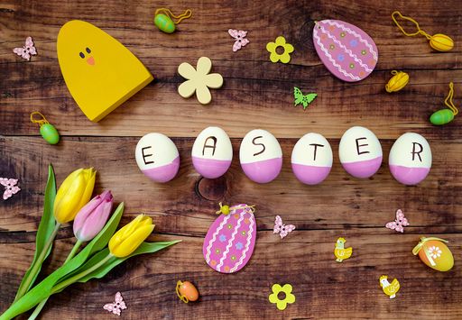 A top view of colorful eggs spelling "EASTER" on the table with tulips on it