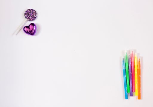 The view of colorful pens, a purple heart and a lollypop over a white surface