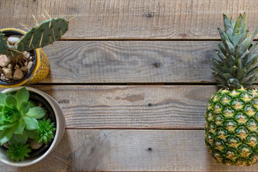 A top view of pineapple and houseplants on a wooden surface - space for text
