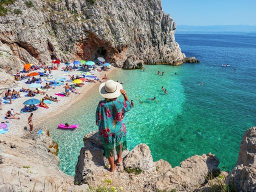 Woman standing on rock above breathtaking Brsec beach in Croatia. People on beach, lifestyle, tourists, tourism, rear view.