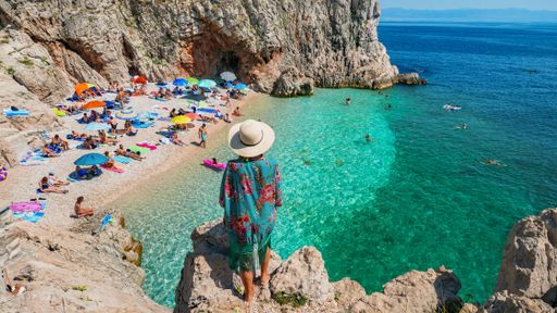 Woman standing on rock above breathtaking Brsec beach in Croatia. People on beach, lifestyle, tourists, tourism, rear view.
