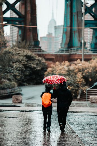 A vertical shot of two people walking together with an umbrella on a rainy day
