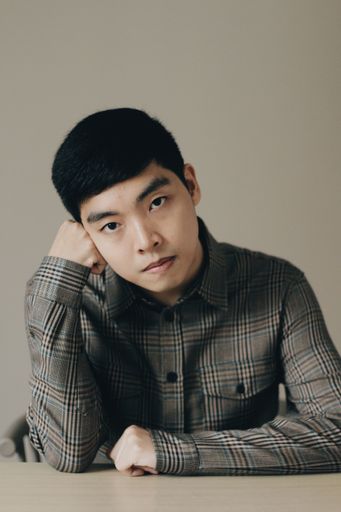 A closeup vertical portrait of a serious attractive Asian man keeping his hand under chin
