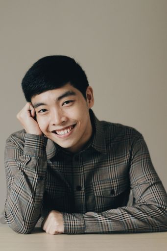 A closeup vertical portrait of a cute happy Asian man leaning his head into his hand
