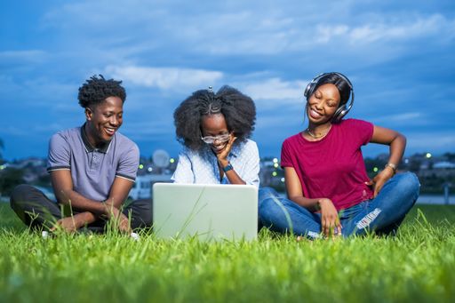 A vibrant shot of three African young people sitting on the grass and looking at a laptop