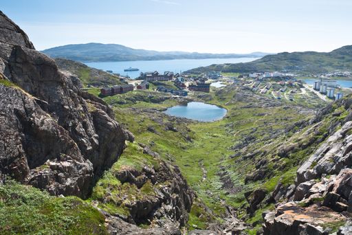 A valley surrounded by rocks and houses with the sea and mountains on the background, Greenland