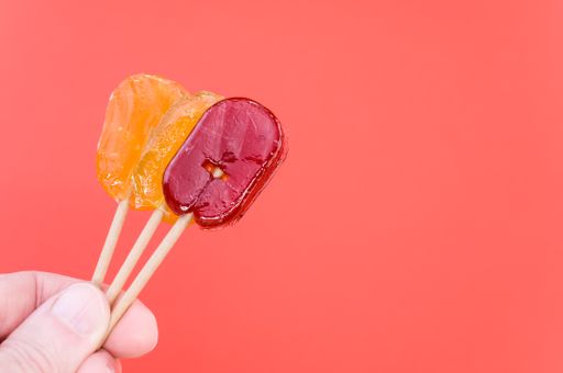 A closeup shot of a hand holding orange and red flavored lollipops isolated on a pink background