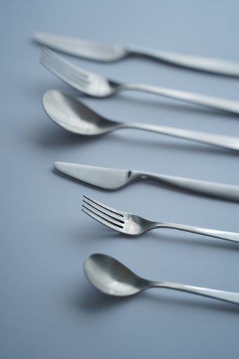 A vertical high angle closeup shot of forks, spoons, and knives on grey background