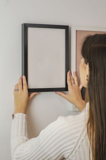 A vertical shot of a woman hanging an empty white-framed paper template on a wall