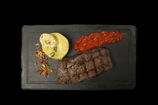 A piece of juicy beef, boiled potato with spiced butter and sauce with pepper and tomato