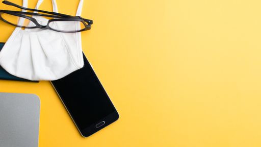 A shot of glasses on a medical mask, a laptop, a charger and a phone