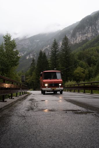 A vertical shot of a Mercedes Benz Custom Van driving on an Italian scenery road with mountains and foggy weather