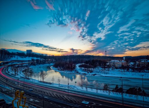 A landscape of roads surrounded by greenery and buildings covered in the snow during sunset