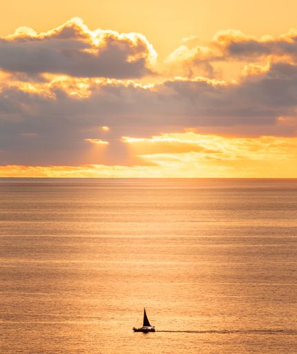 A beautiful view of a lonely boat in the middle of sea during orange sunset