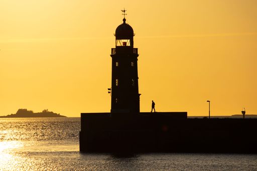 A scenic view of a person standing next to a lighthouse during a breathtaking sunset