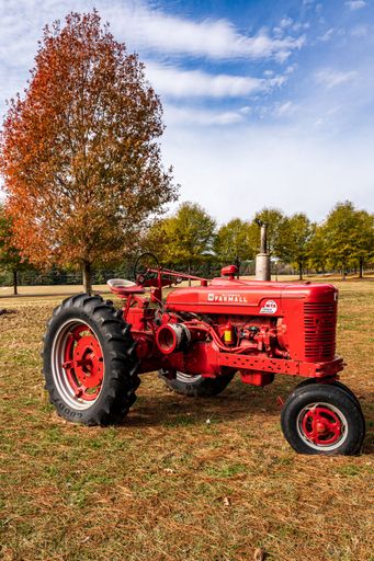 A red "Mccormick Farmall" tractor parked in a grassy field, vertical shot