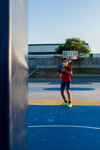 A vertical shot of a boy playing basketball wearing a sanitary mask-concept of the new normal