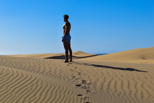 A young male walking alone in the desert with footprints behind