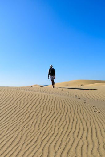 A vertical shot of a young male walking alone in the desert with footprints behind