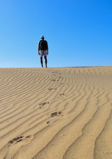 A vertical shot of a young male walking alone in the desert with footprints behind