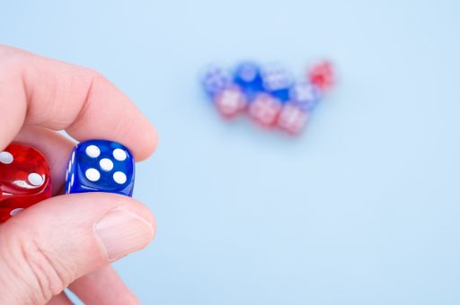 A closeup shot of a hand holding red and blue dice isolated on light blue background