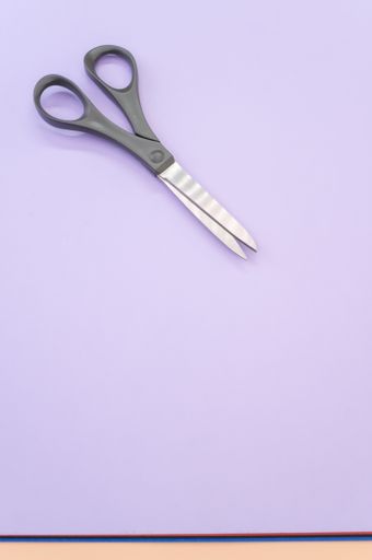 A vertical shot of black scissors isolated on light violet background