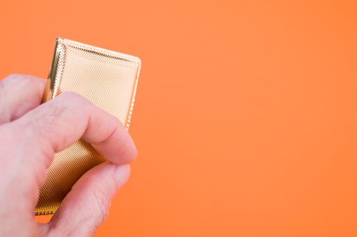 A closeup shot of a hand holding gold miniature bag isolated on an orange background