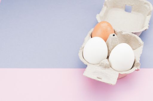 A high angle shot of organic fresh eggs on a tray isolated on pink and blue background