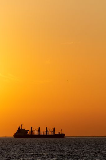 Big cargo ship going through Uruguay river canal at dusk over an orange sky in Conchillas, Colonia, Uruguay