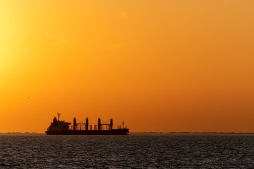Big cargo ship going through Uruguay river canal at dusk over an orange sky in Conchillas, Colonia, Uruguay. Image has horizontal orientation