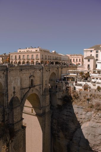 a vertical shot of bridge on a gorge with white buildings and cliffs