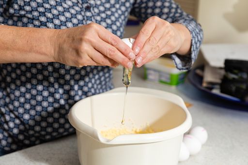 A closeup of a person cracking an egg in a pot for cream in a kitchen