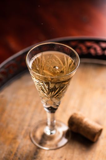 A top view of a glass of white wine and a bottle cork on a wooden tray on the table with blur background