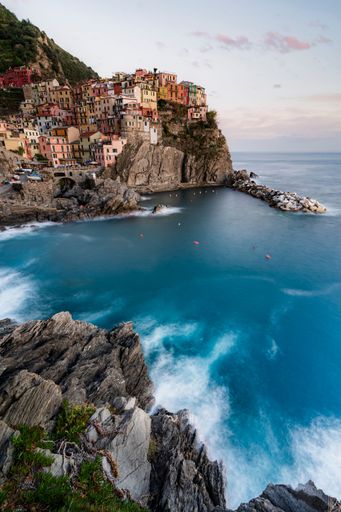 A vertical shot of deep blue water with a view of Manarola town built on a rock in Italy in the daytime