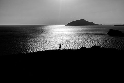 A grey scale shot of a person standing on the hills by the beautiful ocean