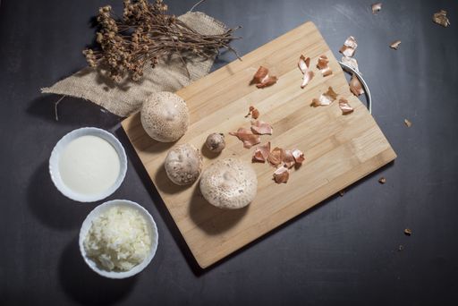 A top view of fresh white mushrooms on a wooden cutting board with chopped onions and sauce in bowls