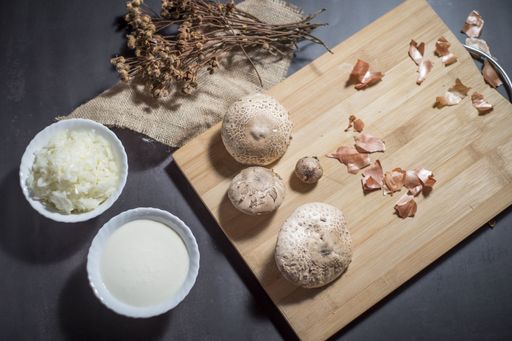 A top view of fresh white mushrooms on a wooden cutting board with chopped onions and sauce in bowls
