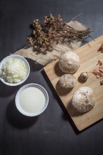 A top view of fresh white mushrooms on a wooden cutting board with chopped onions and sauce in bowls