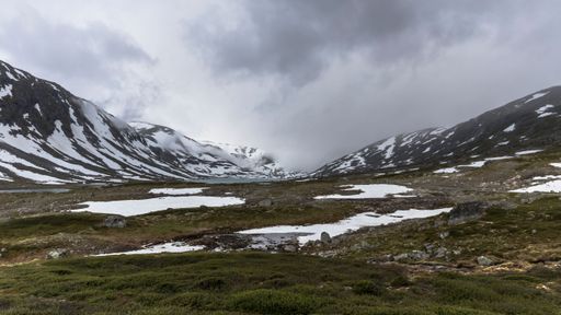 A snowy meadow against the background of mountains and cloudy sky. Norway.