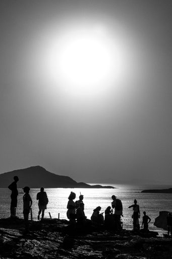 A vertical grey scale shot of a group of people standing on the beach by the sea