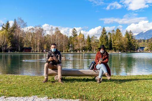 A beautiful shot of the male and female using their mobile phone while sitting on both ends of the bench near the pond