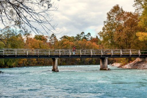 A beautiful shot of a female standing in the middle of the bridge while watching the flowing river water