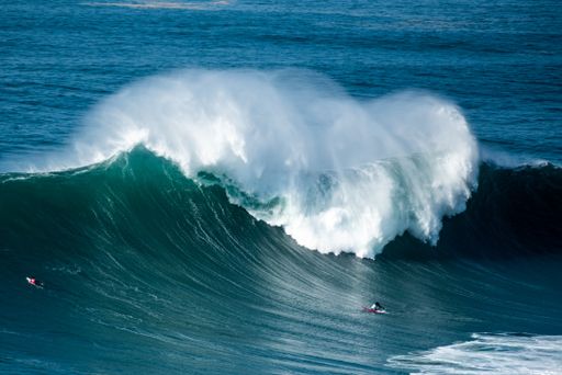 The big foamy waves of the Atlantic Ocean near the Nazare municipality in Portugal and surfers riding