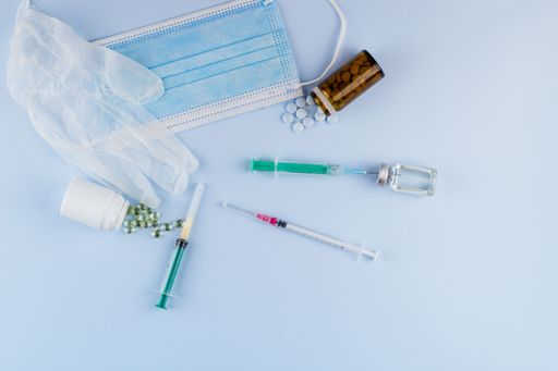 Top view of syringes, blue hygienic protective mask, gloves, tablets and glass medicine bottle ready for use. Pandemic and health concept.