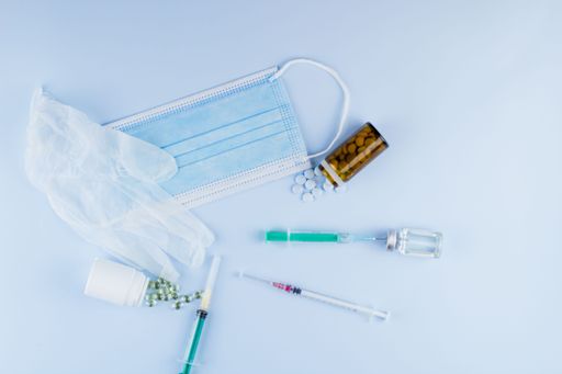 Top view of syringes, blue hygienic protective mask, gloves, tablets and glass medicine bottle ready for use. Pandemic and health concept.